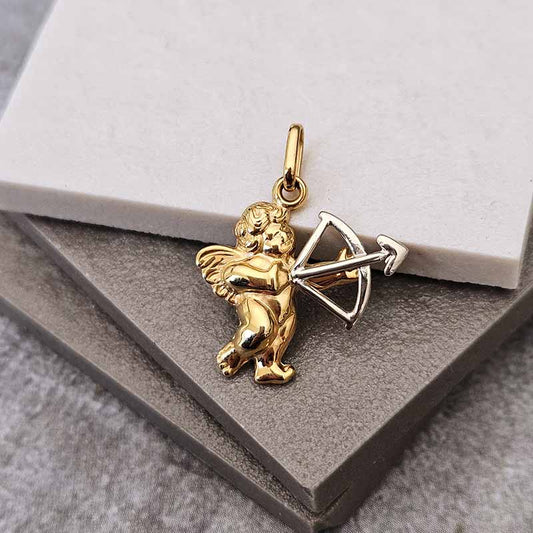 A gold cupid pendant holding a silver bow and arrow, displayed on a gray textured surface with a white marble block.