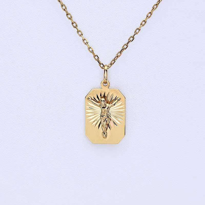 A gold crucifix pendant necklace on a delicate chain, displayed against a clean, light off-white background.