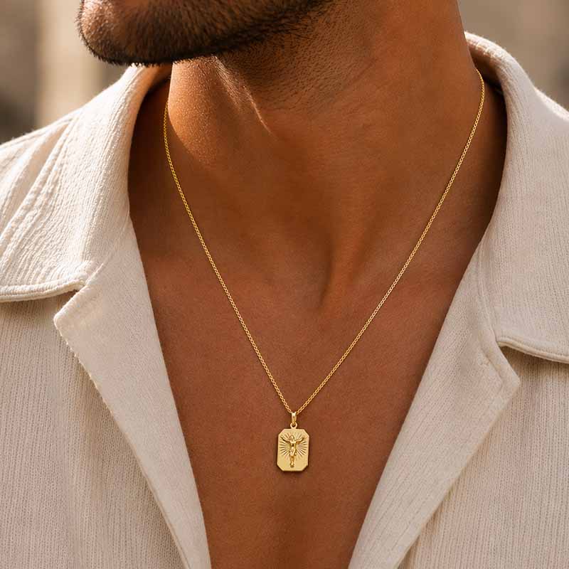 A close-up lifestyle shot of a man wearing a gold chain necklace with a rectangular pendant featuring a figure of Jesus, styled with a cream-colored shirt.
