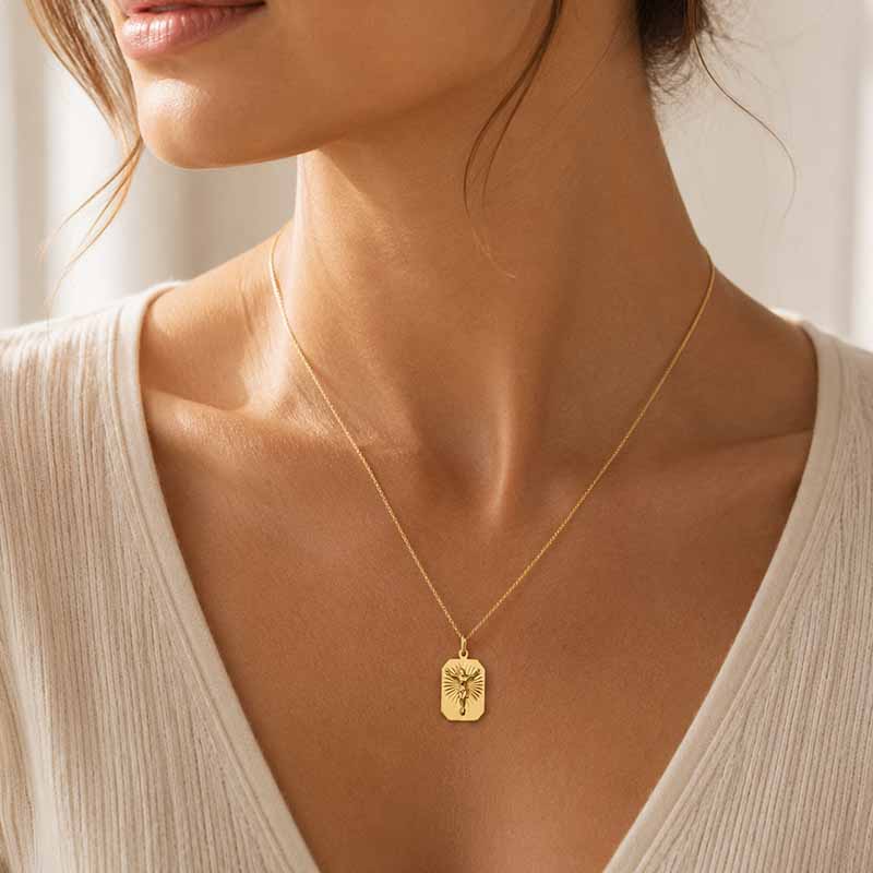 A close-up of a woman wearing a delicate gold necklace with a small rectangular pendant featuring a figure of Jesus