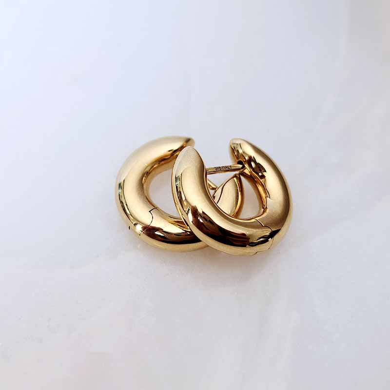 A pair of polished gold hoop earrings with a glossy, reflective finish, resting on a clean white surface.