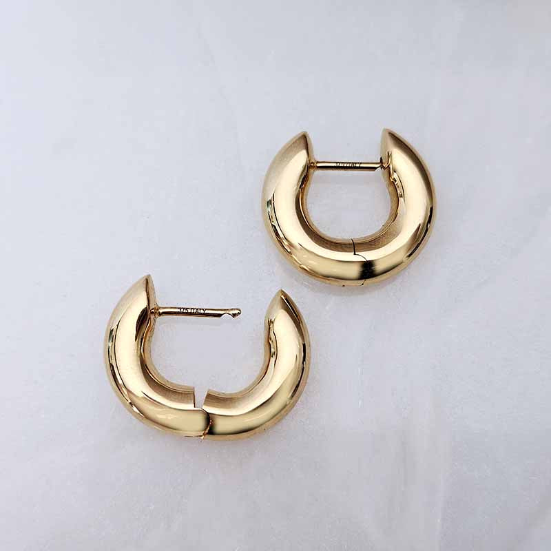 A pair of polished gold huggie hoop earrings on a light gray textured background.