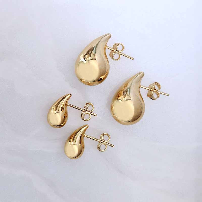 Four gold teardrop-shaped stud earrings with butterfly backings, arranged on a light gray marble surface.