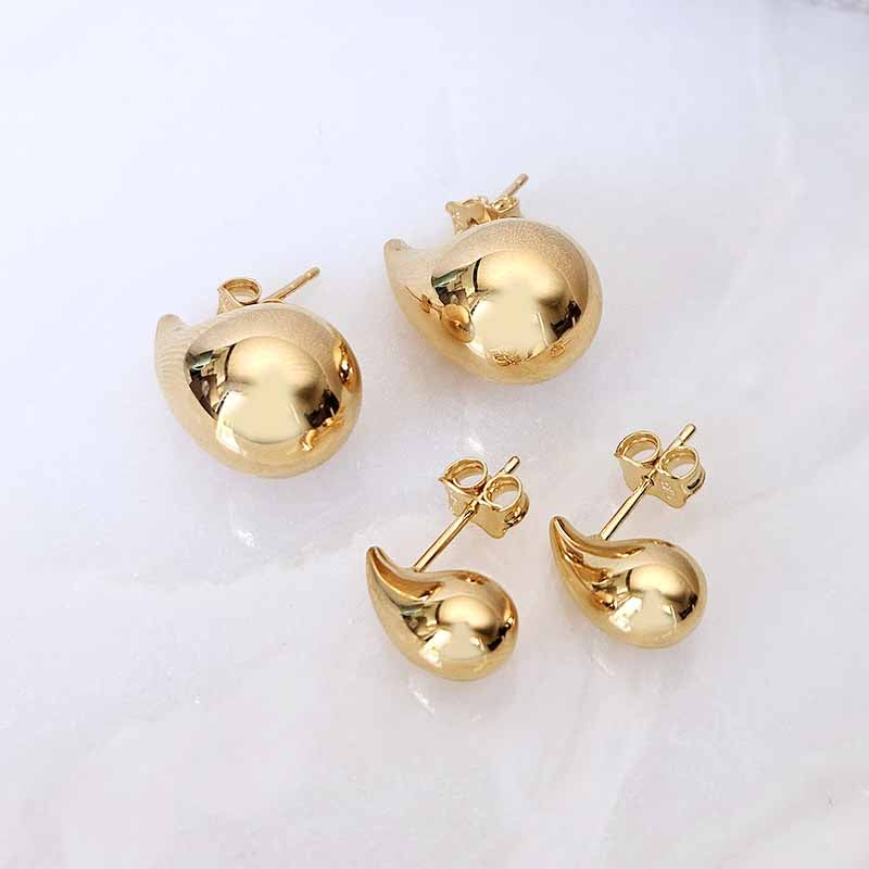 Four gold-toned stud earrings arranged on a light white background, including two larger round dome-shaped studs and two smaller teardrop-shaped studs with visible posts and backing.