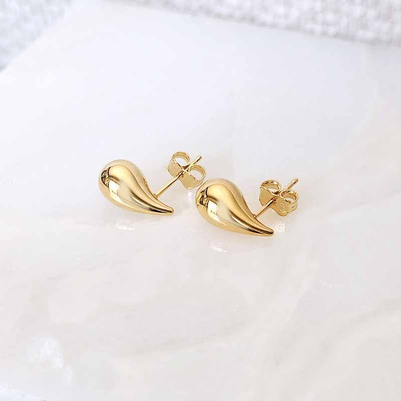 A pair of gold teardrop-shaped stud earrings with butterfly backings, displayed on a white marble surface.