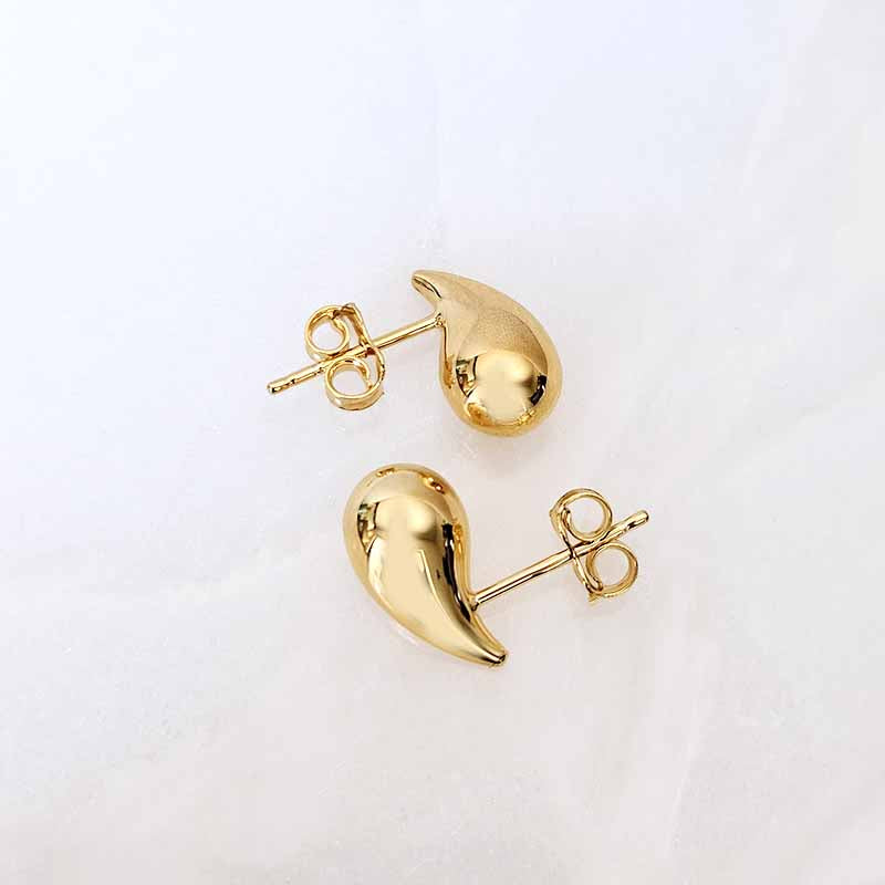 A pair of gold teardrop-shaped stud earrings with butterfly backings, displayed on a clean white textured surface.