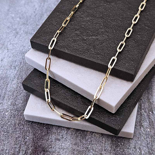A gold paperclip chain necklace draped over a stack of black and white display blocks on a textured gray surface.