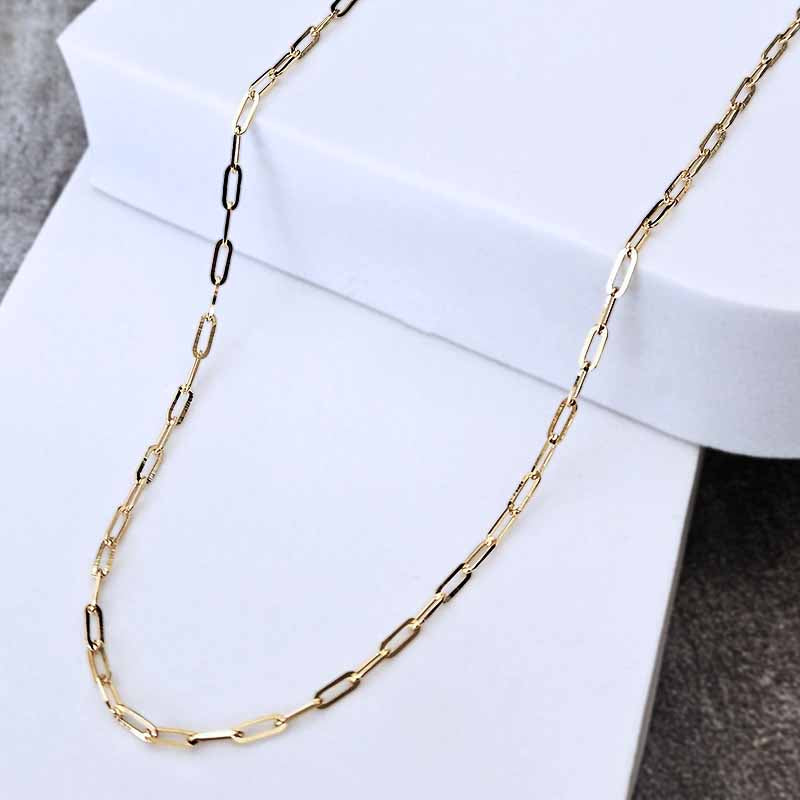 A gold paperclip chain necklace draped over a white display block, showing polished oval links on a clean studio background.
