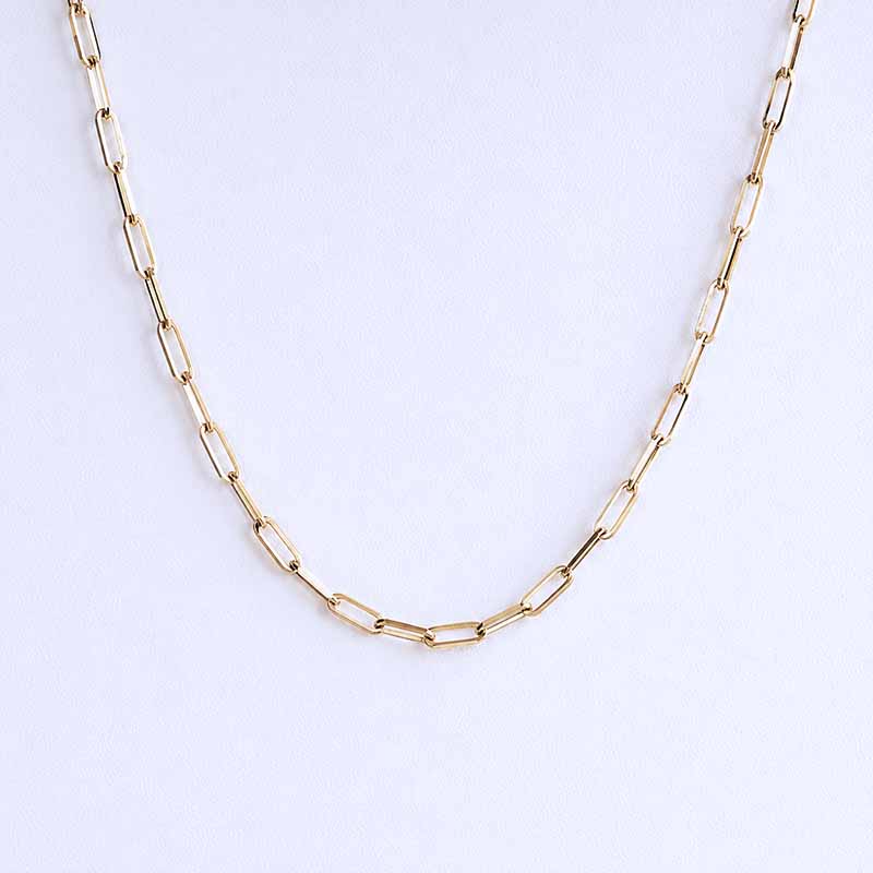 A gold paperclip chain necklace draped in a U-shape against a clean, light off-white background.