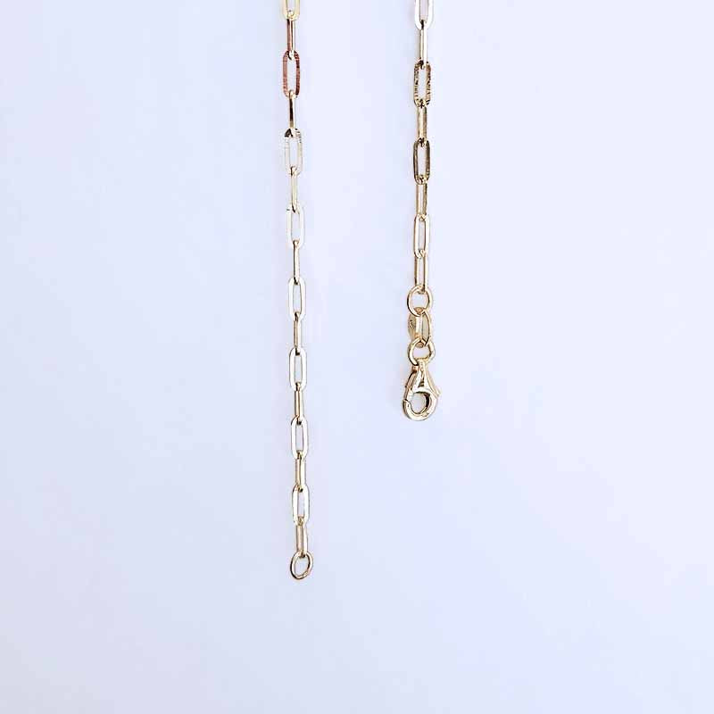 A close-up of a gold paperclip chain necklace, showing the delicate links and lobster clasp against a light blue background.