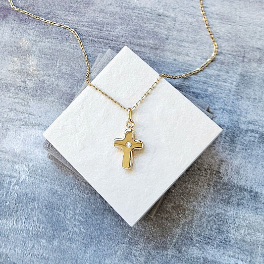 Gold cross necklace on a white card with a gray background