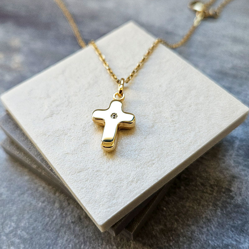 Gold cross necklace on a white card with a gray background