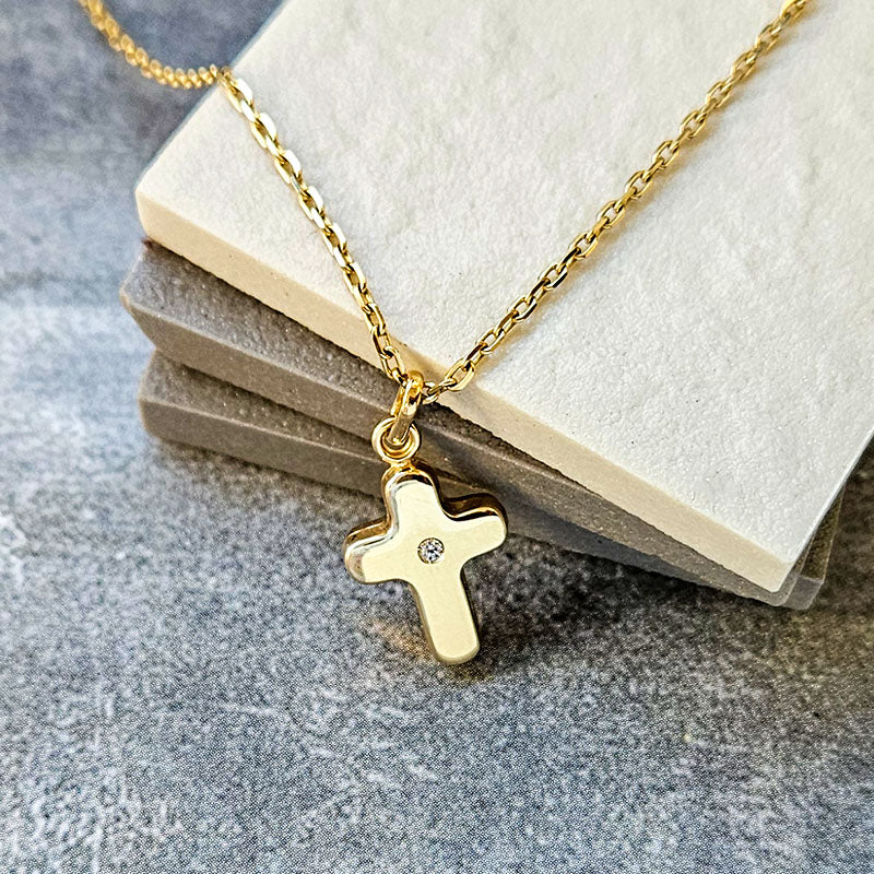 Gold necklace with a cross pendant on a textured surface