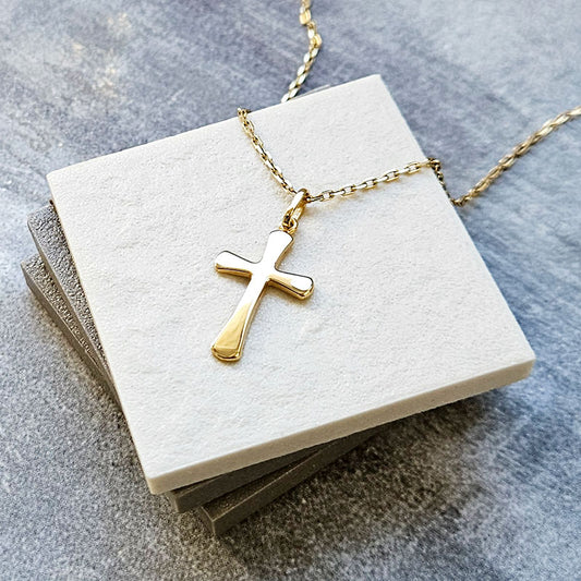 Gold cross necklace on a white card with a gray background