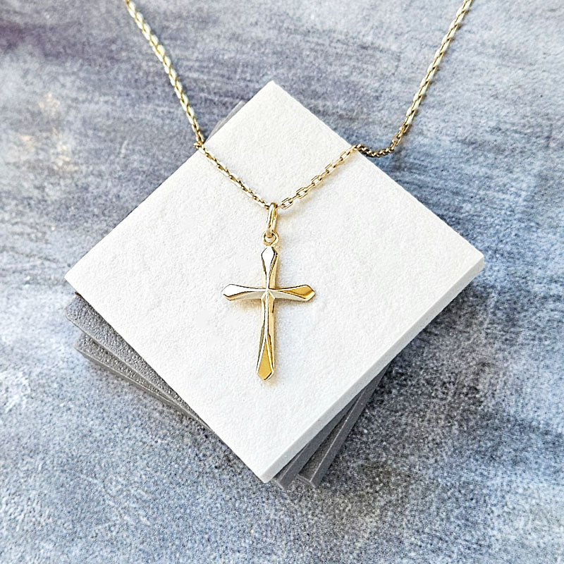 Gold cross necklace on a white card with a gray background