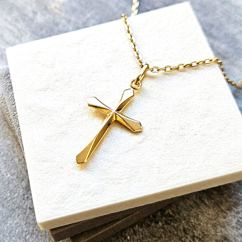 Gold cross necklace on a white card with a gray background