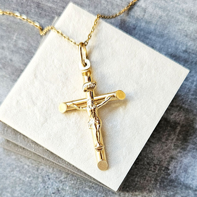 Gold crucifix pendant on a white card with a gray background