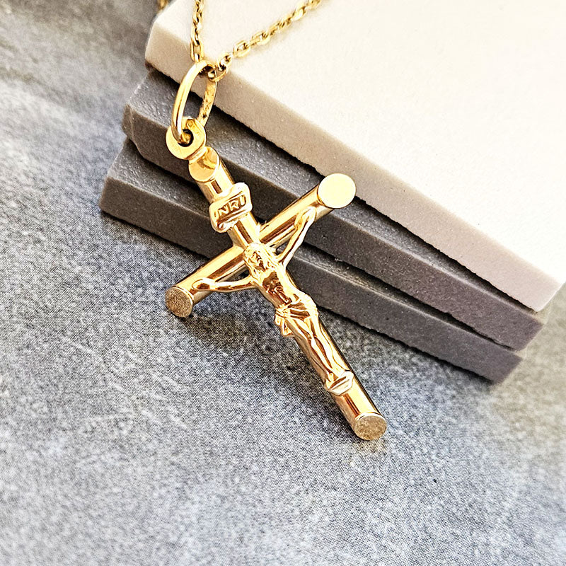 Gold crucifix pendant on a chain against a gray textured background