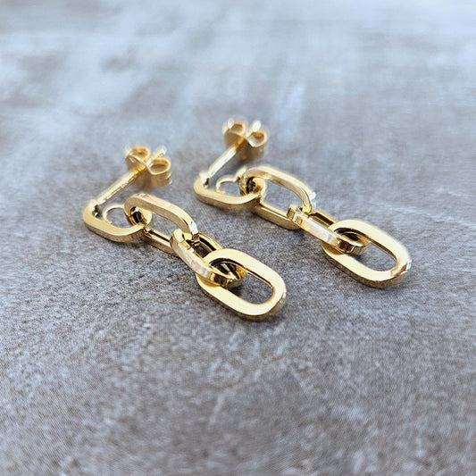 Gold chain-style earrings on a textured gray surface