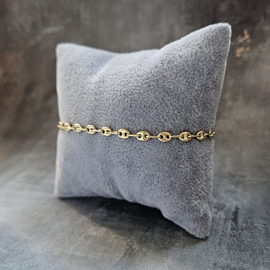 Gold chain bracelet on a gray textured pillow against a dark background