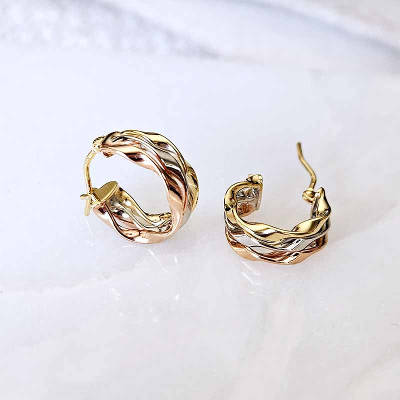 A pair of gold hoop earrings with a twisted, braided design, displayed on a light marble surface.