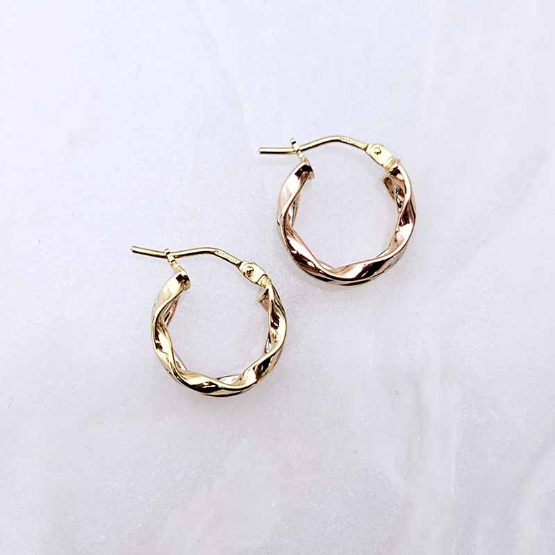 A pair of gold hoop earrings with a twisted, textured finish, displayed on a light gray marble surface.