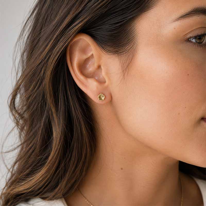A close-up of a woman's ear wearing a small gold flower stud earring.