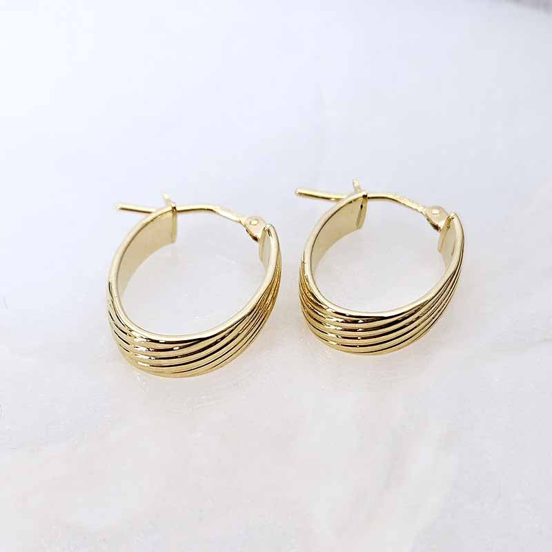 A pair of gold hoop earrings with multiple parallel horizontal bands, displayed on a clean, light off-white surface.