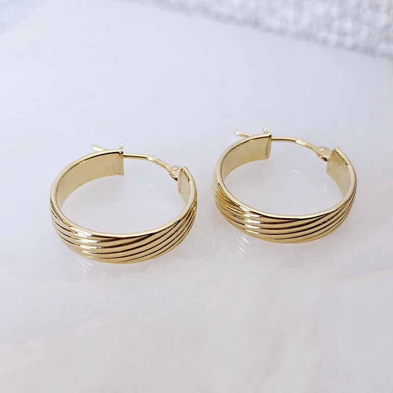 A pair of gold hoop earrings with a multi-strand horizontal ribbed design, displayed on a light marble surface.