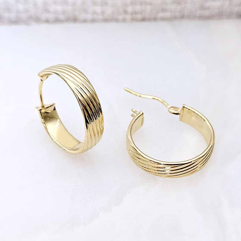 A pair of gold hoop earrings with a textured, ridged band design, displayed on a light white surface.