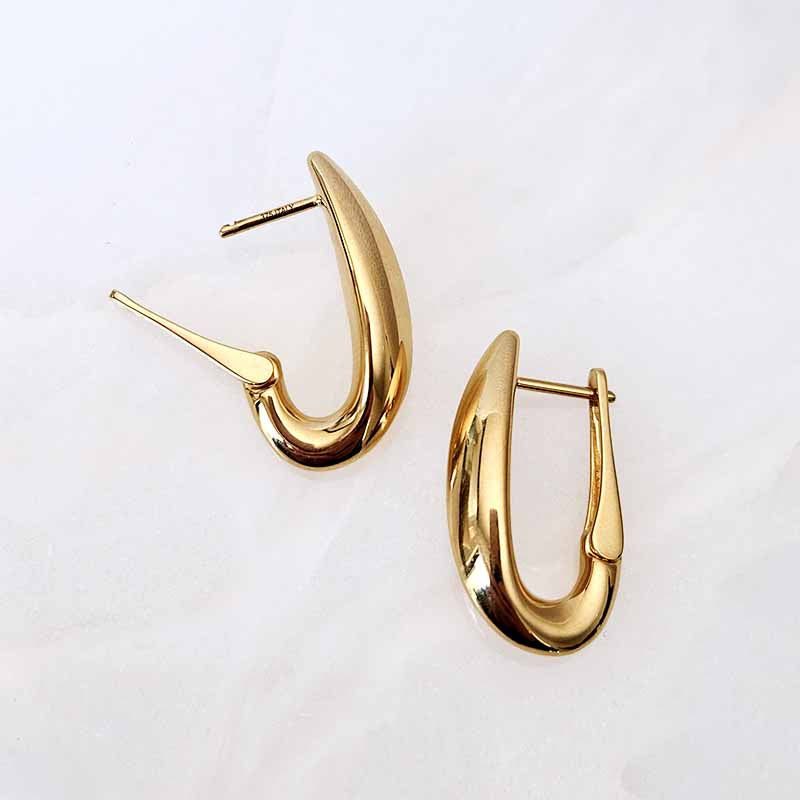 A pair of gold-toned, curved hoop earrings with a polished finish, displayed on a light, textured white background.