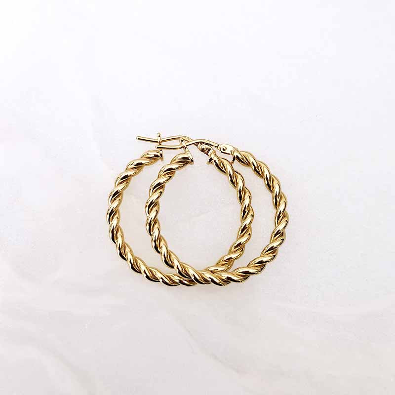 A pair of gold hoop earrings with a twisted rope design, displayed on a light, slightly textured white background.