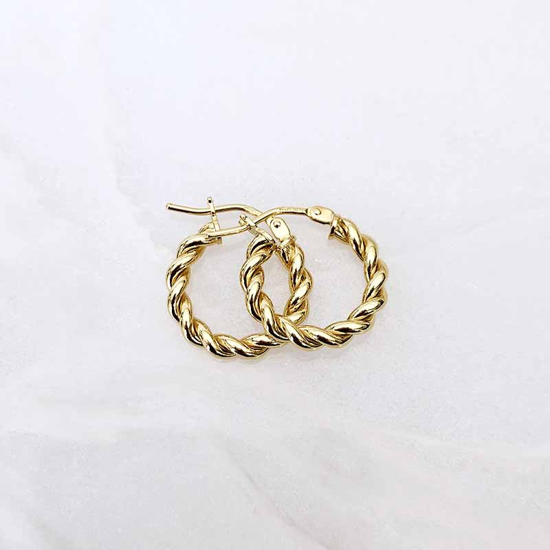 A pair of gold hoop earrings with a twisted rope texture, displayed on a light, slightly textured white background.