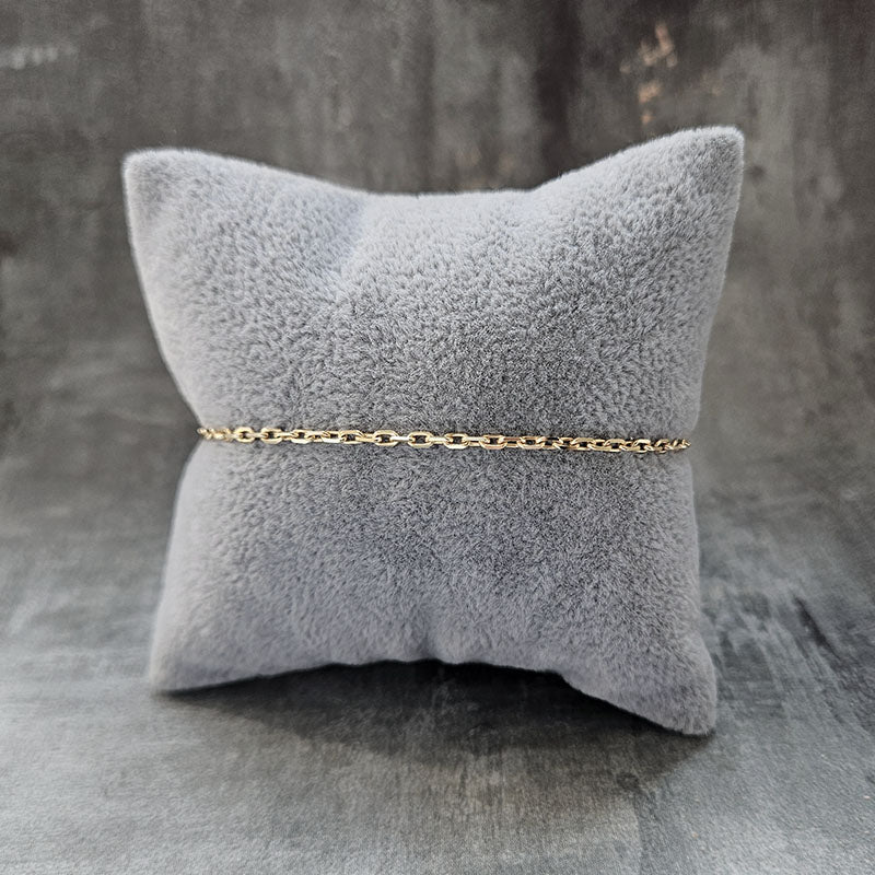 Gold chain bracelet on a gray textured pillow against a gray background