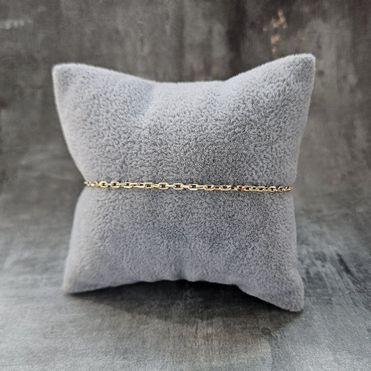 Gold chain bracelet on a gray textured pillow against a gray background