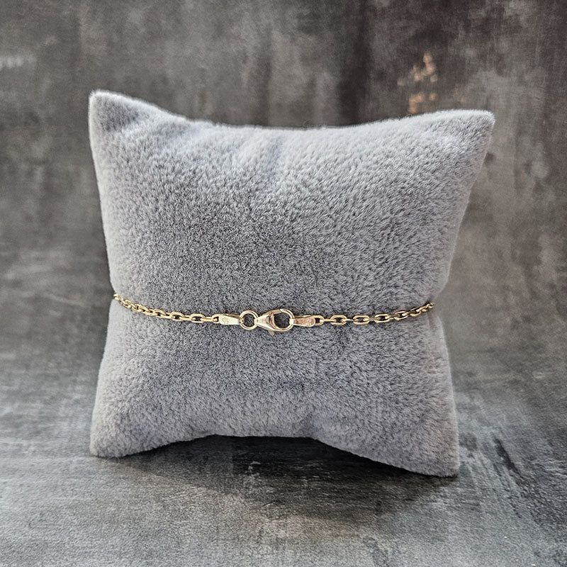 Gold chain bracelet on a gray textured pillow against a gray background