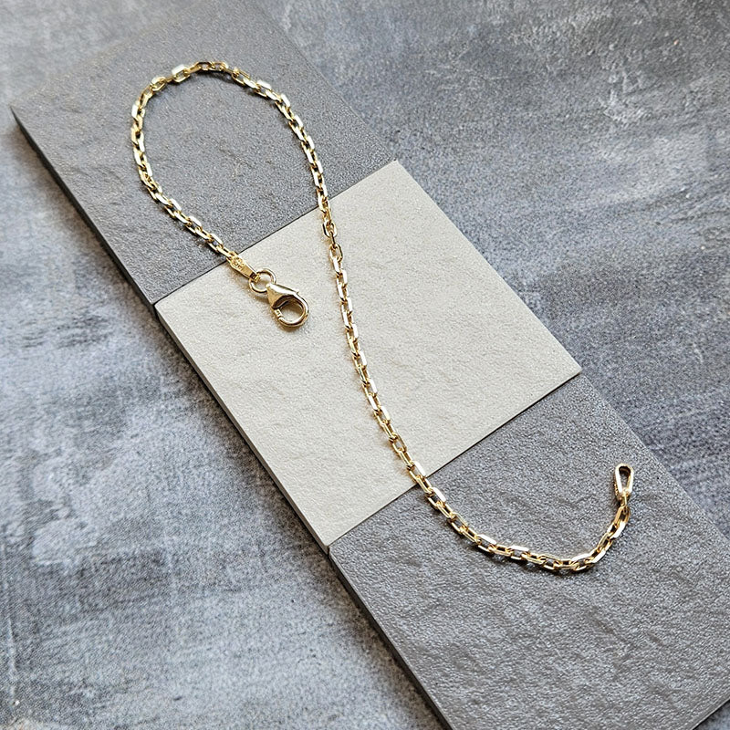 Gold chain bracelet on a gray surface with a neutral card