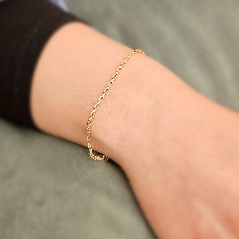 Gold bracelet on a person's wrist against a neutral background