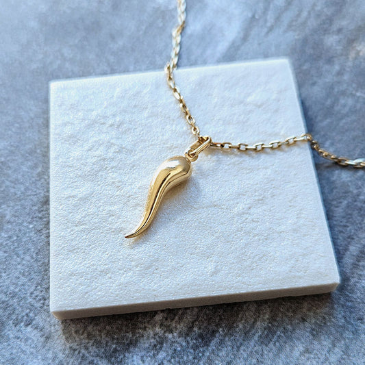 Gold necklace with a unique pendant on a white square base against a gray marble background