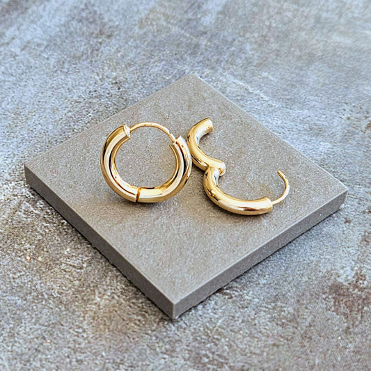 Gold hoop and crescent moon earrings on a gray stone surface