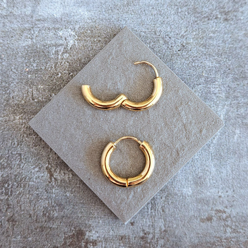 Gold hoop earrings on a gray stone surface