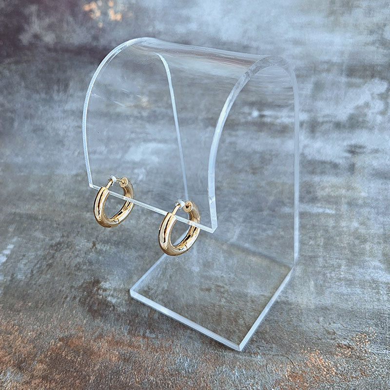 Gold hoop earrings on a clear stand against a textured gray background