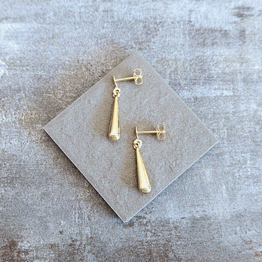 Gold earrings on a gray textured surface