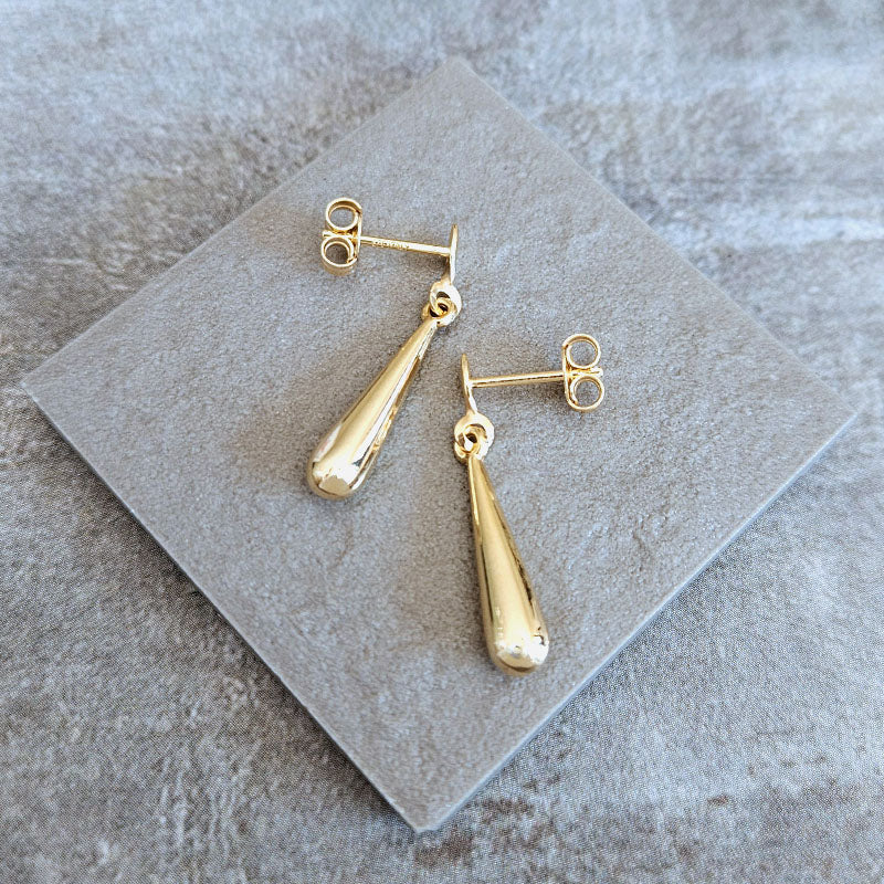 Gold teardrop earrings on a gray stone surface