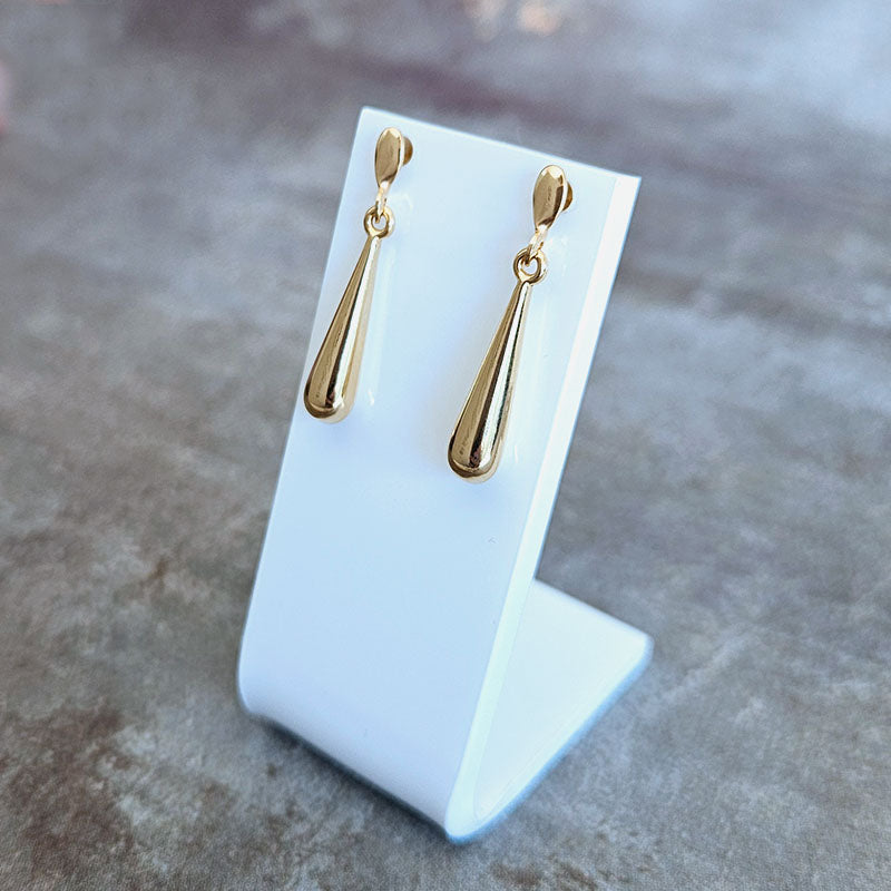 Gold teardrop earrings on a white stand against a gray background