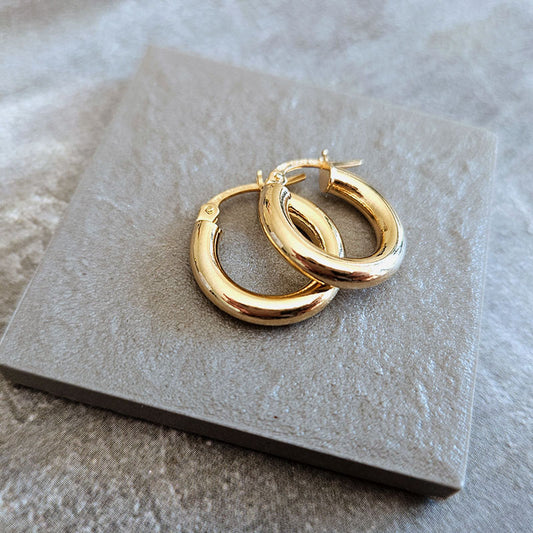 Gold hoop earrings on a textured stone surface