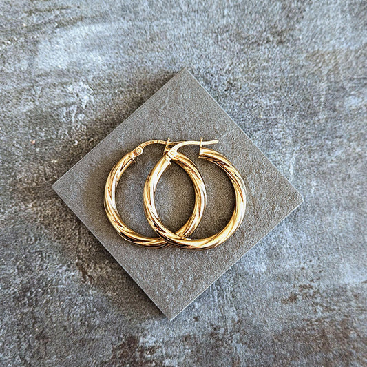 Gold hoop earrings on a textured stone surface