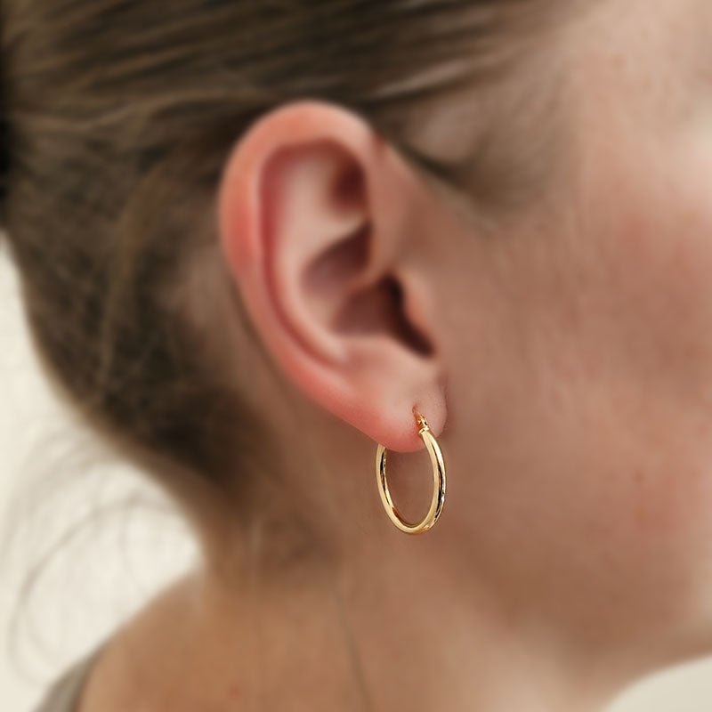 Close-up of a person wearing a gold hoop earring with a blurred background