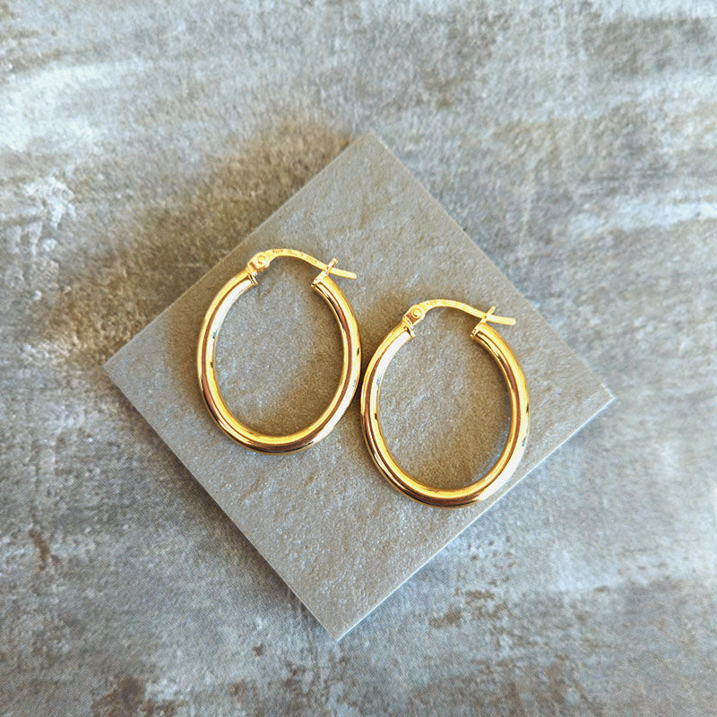 Gold hoop earrings on a beige stone surface