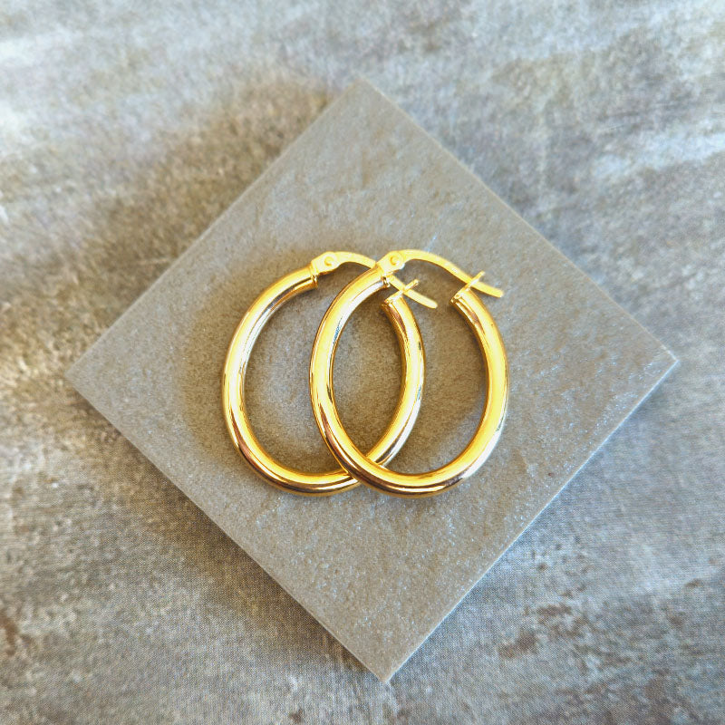 Gold hoop earrings on a beige card with a textured background